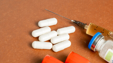 A bottle of medicine with a syringe next to it. The syringe is yellow and has a blue cap. The pills are white and are scattered on the table