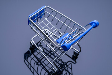 A shopping cart with a blue handle is sitting on a black surface. The cart is empty and has a silver frame