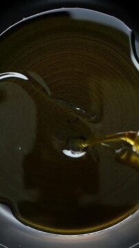 Close up of golden extra virgin olive oil pouring from bottle neck into dark frying pan