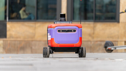 A robot is standing on the sidewalk. It is purple and red. The robot is not moving