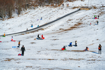 Crowded snowy hill with families and children sledding and playing outdoors. Winter recreation area at Ski resort Platak, Croatia