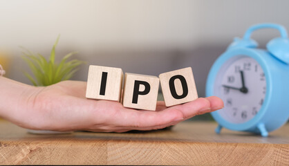 A hand holds three wooden blocks spelling IPO against lithe background