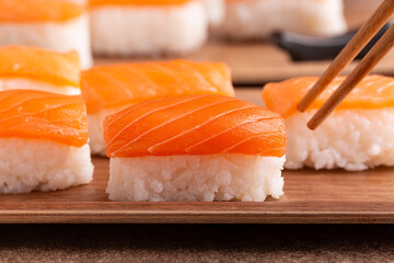 Eating salmon sushi nigiri with chopsticks, brown, beige background. Close up.