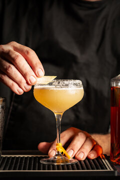 Preparing a margarita cocktail in a bar. Cold drink consisting of tequila, triple sec, and lime juice, served with salt on the rim of the glass.  Black background, vertical image.