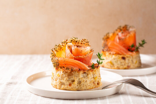 Smoked  salmon and vegetable flan or sformatino,  made with cauliflower, leek, egg, ricotta and parmesan cheese. Monoportion appetizers on a white plate, beige background.