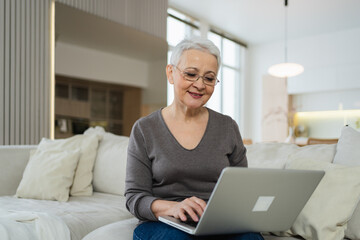 Confident stylish happy middle aged senior woman using laptop at home. Stylish older mature 60s...