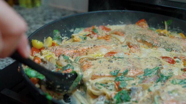 chef stirring creamy salmon with spinach and tomatoes in a skillet