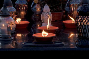 Świece palące się na nagrobku w noc Wszystkich Świętych. Świece i lampiony zapalane , symbolizują pamięć. Scena przedstawia czerwone kielichy ze świecami, z których niektóre delikatnie migoczą. © Grzegorz