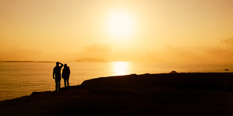 Couple of tourists at Dunquin or Dun Chaoin pier, Ireland's Sheep Highway. Pathway winding down to the pier, ocean coastline, cliffs. Popular location on Slea Head Drive and Wild Atlantic Way. © MNStudio