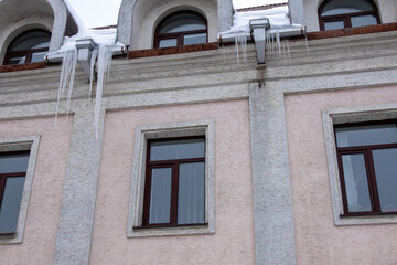 Obraz premium Snow and ice form icicles hanging from the roof of a building with windows in winter season
