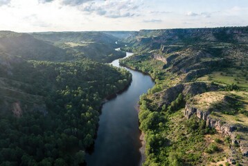 Aerial view of a winding river cutting through lush green valleys and rugged cliffs