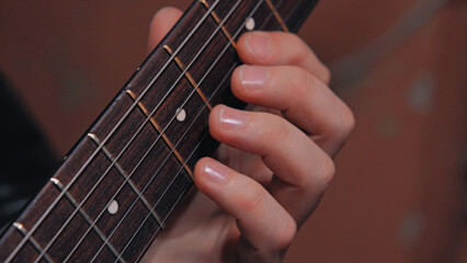 Obraz premium Extreme close-up of a guitarist's fingers fretting a chord on a dark wood fretboard. Warm lighting highlights the focused musical practice. Diagonal composition creates a dynamic feel