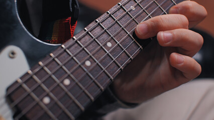 Fototapeta premium Extreme close-up of a guitarist's hand playing a chord on a dark wood fretboard. The focused shot highlights the musician's fingers pressing the strings. Concept of practice, skill, music creation