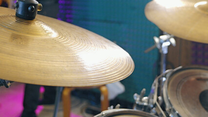 Obraz premium Close-up view of a golden cymbal on a drum set, reflecting bright stage lights. The colorful blue and purple background creates a vibrant, energetic mood for a concert or live performance