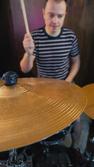 Obraz premium Focused drummer playing in a dark studio. A shiny brass cymbal is in the foreground with the musician blurred behind. Low-angle shot conveying energy, passion, and musical performance