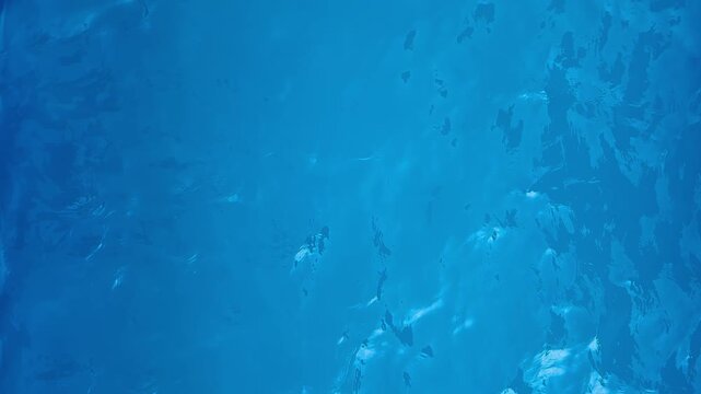 Top-down view of a swimming pool water surface with ripples and sun reflections. Dynamic abstract composition suitable for both horizontal and vertical use. 4k 60fps, High frame rate 