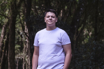 A teenager stands outdoors, wearing a white t-shirt and a slight smile.