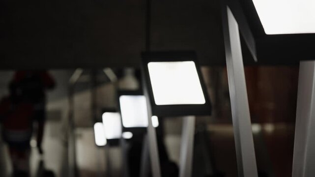 Row of glowing lightbox screens on sleek stands lining a dim interior corridor, creating a moody, modern pathway with deep perspective and a human silhouette in the background