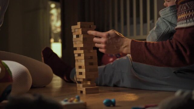A loving family, comprising mom, dad, and young daughter, bonds over a thrilling game of Jenga on the cozy living room floor, basking in the serene ambiance of a warm home on a peaceful evening