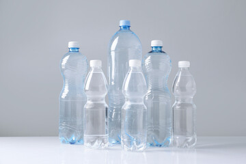 Naklejka premium Water bottles of different sizes on white table against grey background