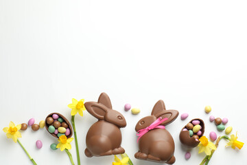 Naklejka premium Chocolate Easter bunnies, flowers, ribbon and eggs on white background, flat lay. Space for text