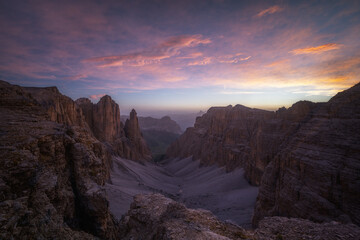 Stunning wide-angle view of rugged Dolomite peaks and a deep scree valley under a vibrant sunset sky. Ideal for travel and outdoor adventure media.