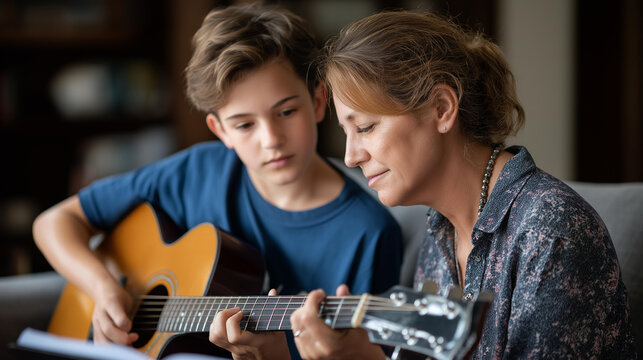 Faceless music teacher and teenage student sitting on sofa learning to play guitar in private lesson in living room at home musical instruction domestic education with copy