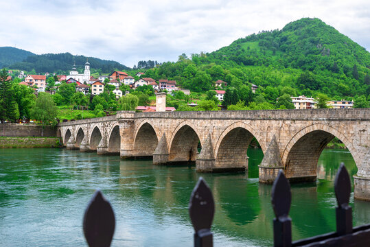Ottoman stone bridge in Visegrad, Bosnia and Herzegovina, crossing the Drina River with arches reflected in clear green water.