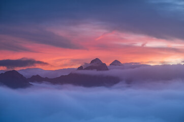 Fototapeta premium Stunning high-altitude landscape featuring mountain peaks above a thick cloud layer under a vibrant purple and orange sunset. Ideal for travel and environmental themes.