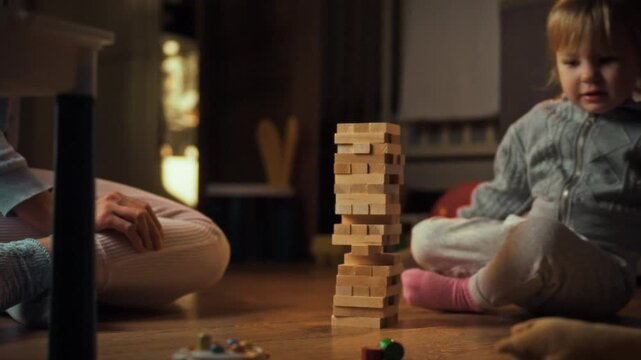 Young daughter her mother sit on floor, engrossed warm evening play session, constructing delicate tower from wooden Jenga blocks, fostering interactive learning fun through challenging balance game