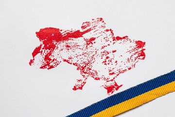 Naklejka premium The outline of the map of Ukraine, drawn in red paint and the ribbon of the Ukrainian flag on a white background
