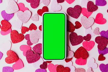 Happy Valentine's day digital mockup. Blank phone screen with space for text and stylish pink and red hearts flat lay on pink paper background. Smartphone love template