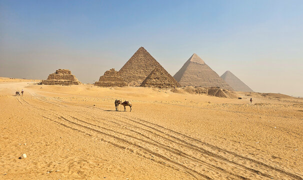 Wide panoramic view of the Great Pyramids of Giza under a clear blue sky, showcasing ancient Egyptian architecture and the vast desert landscape near Cairo, Egypt.