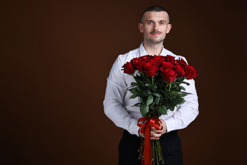 Valentine's day celebration. Man with beautiful bouquet of red roses on brown background, space for...