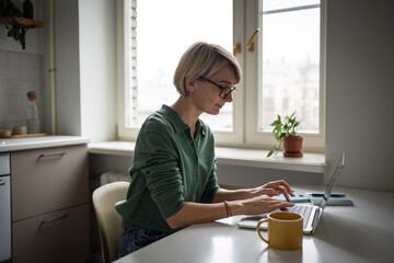 Online entrepreneur woman works on remote from home, sitting at table typing on laptop, finishing...
