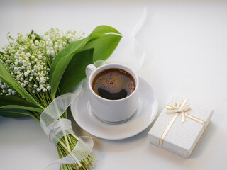 cup of coffee , a bouquet of lilies of the valley and a small gift box on a white background