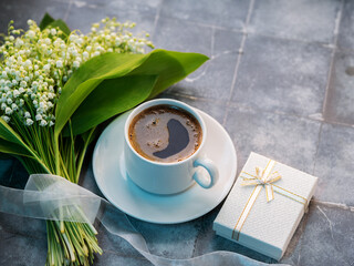 cup of coffee on the table with a bouquet of lilies of the valley and a white gift box, copy space
