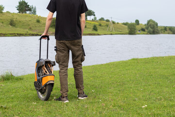 man holds an electric unicycle by a sliding handle . Eco-friendly transport, nature background