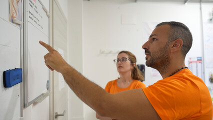 Young man and woman reviewing upcoming electrical service tasks on company whiteboard