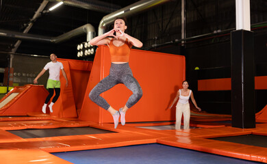 Positive middle-aged woman in sporty clothes jumping vertical high in modern trampoline hall