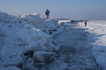 Ice toros (mountains of piled-up ice) on the beach in Mikoszewo, Baltic Sea, Pomerania, Poland. This is a very interesting and rare phenomenon. Silhouettes of people walking and taking photos.
