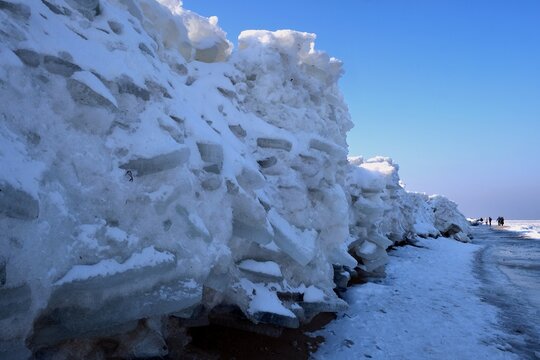 Ice toros (mountains of piled-up ice) on the beach in Mikoszewo, Baltic Sea, Pomerania, Poland. This is a very interesting and rare phenomenon. Silhouettes of people walking and taking photos.
