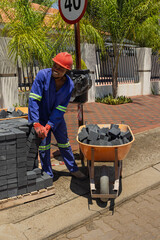 african construction worker laying dark grey brick pavers on residential sidewalk.