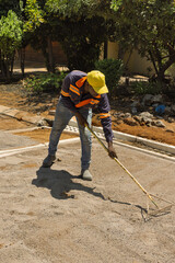 African construction worker raking and leveling a gravel base on a sunny day