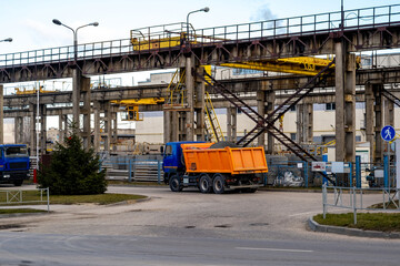 Fototapeta premium Industrial Construction Site With Orange Dump Truck Under Steel Framework And Heavy Machinery In Daylight