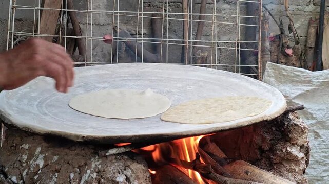 Close-up of female hands placing handmade corn tortilla on a hot clay comal, traditional cooking.