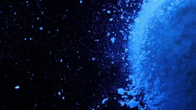 Abstract Macro Motion of Blue Crystal Particles on Black Background. Bright sphere. Colourful pill.