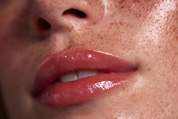 Fototapeta premium Close-up of a person's lips. The lips are glossy and well-defined, with a hint of a smile. The skin around the lips is visible with some freckles. 