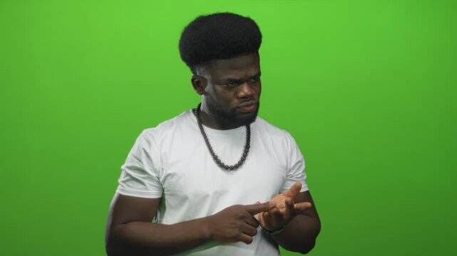 Man in white t shirt points finger to palm while wearing beaded necklace in studio; concentration counting numbers.