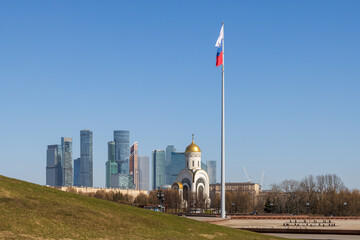 Obraz premium View of the flagpole with the Russian flag. Church against the backdrop of high-rise buildings. St. George's Church and skyscrapers of the Moscow International Business Center. Moscow city, Russia.